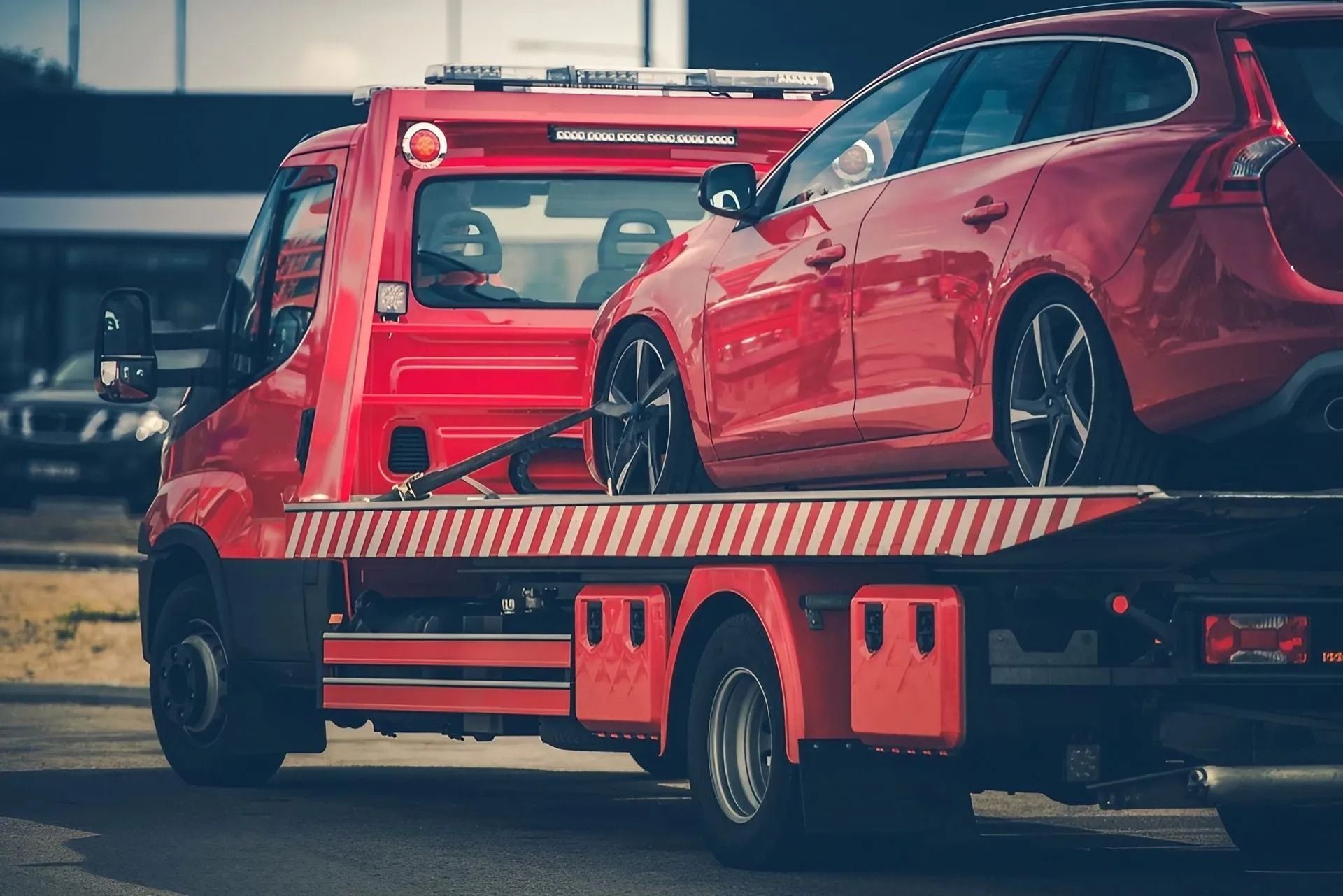 Red Tow Truck Transporting a Red Car on a City Street — Alfie's Towing in Kuranda, QLD