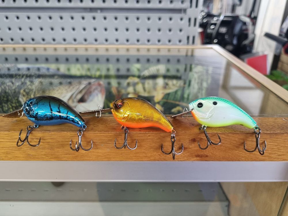 Three Different Colored Fishing Lures Are Sitting On A Shelf — Posties Caravans Boats Small Engines Inverell In Inverell, NSW