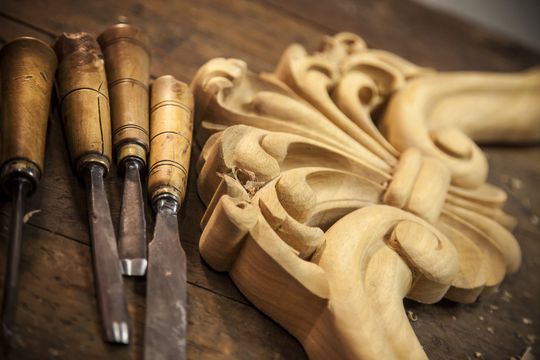 a wood carving is sitting on a wooden table next to a set of carving tools .