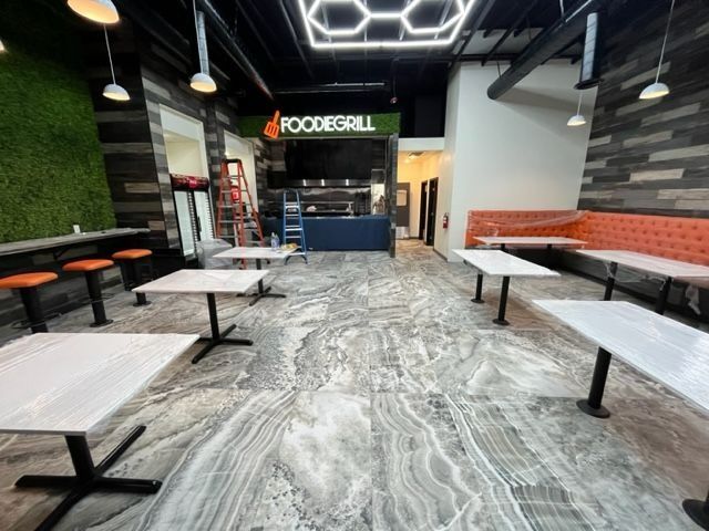 Interior of a restaurant. Tables and seating in orange, gray, and black with a faux-wood accent wall.