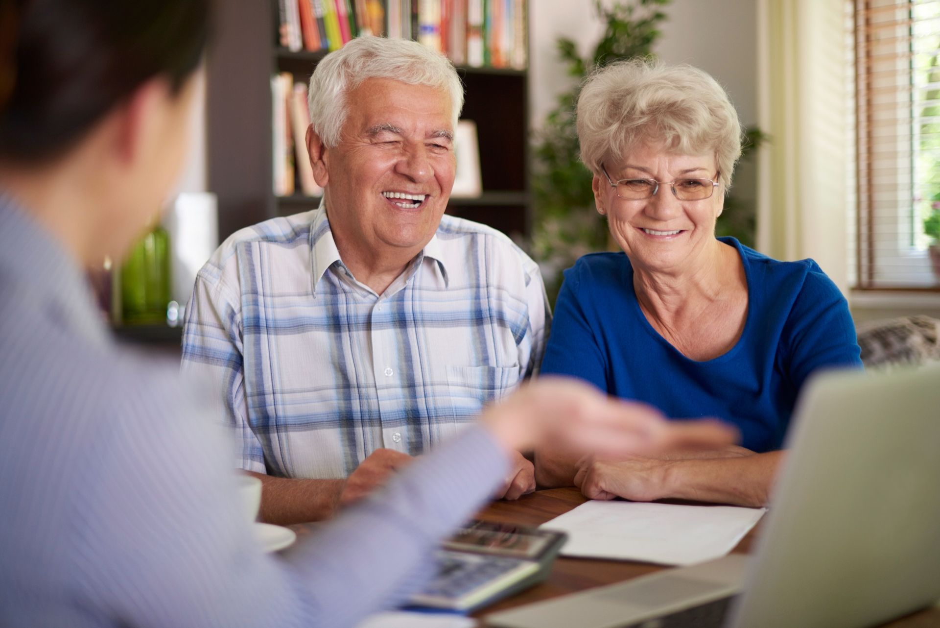 An advisor talks with a couple sitting at a table with a laptop, calculator, and documents in a home setting.