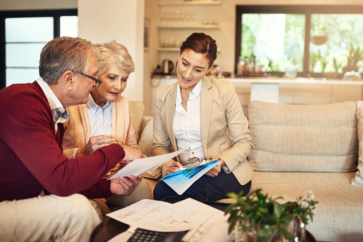 A professional advisor sits with two people in a living room, discussing and reviewing documents together.