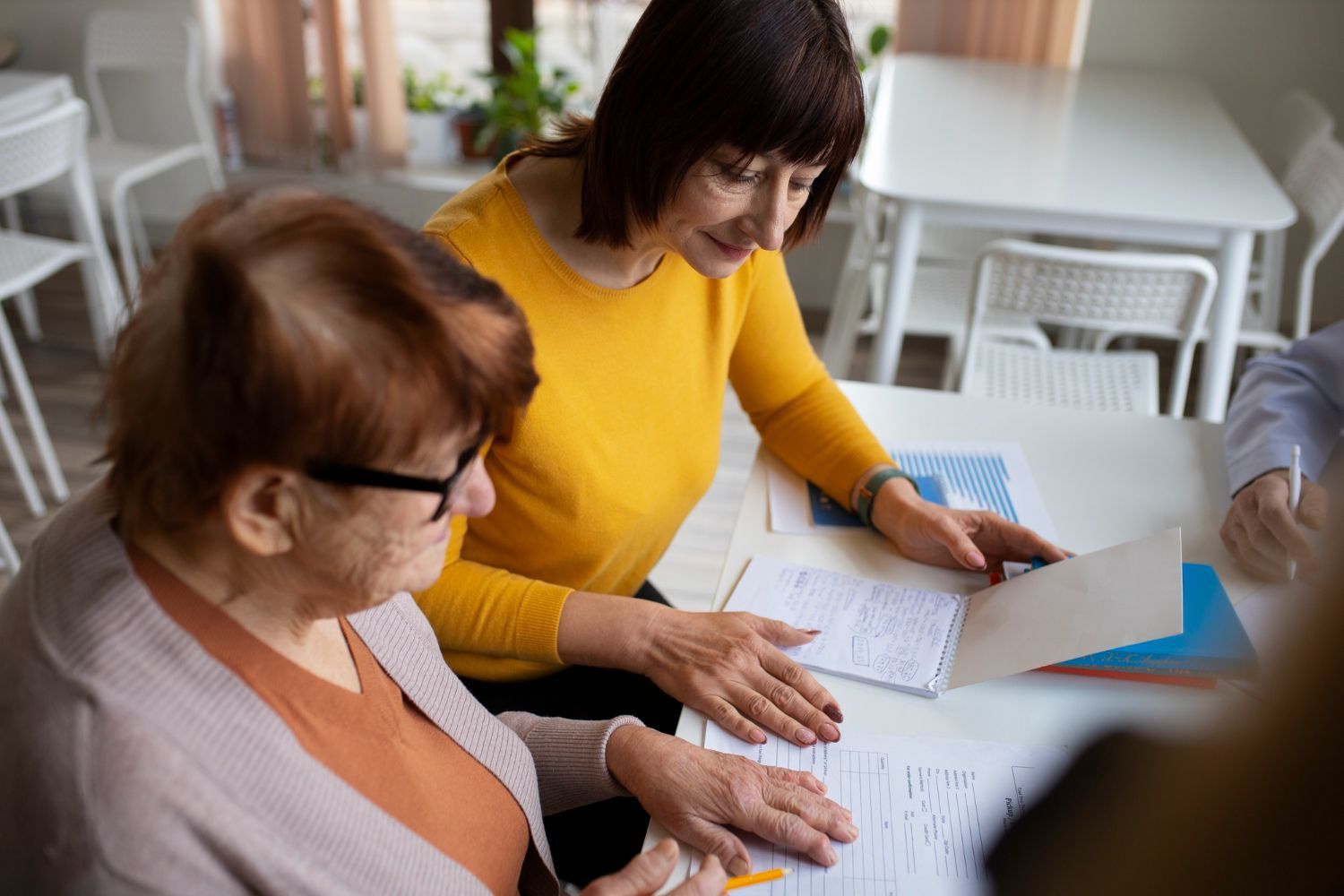 Two people sit at a table, reviewing documents together in a brightly lit room.