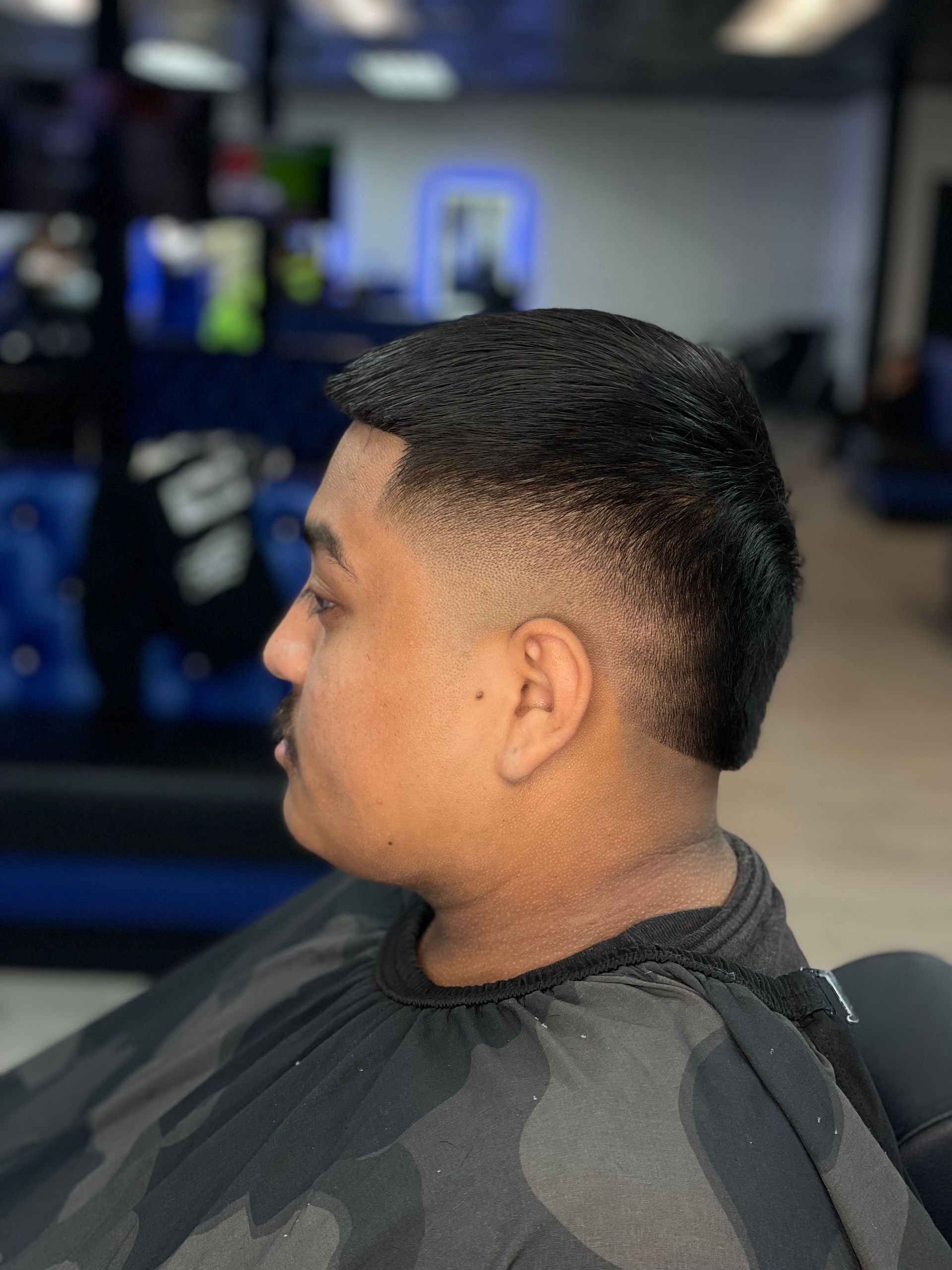 Man with a tapered haircut, fading from skin to dark brown, wearing a barber's cape, profile view.