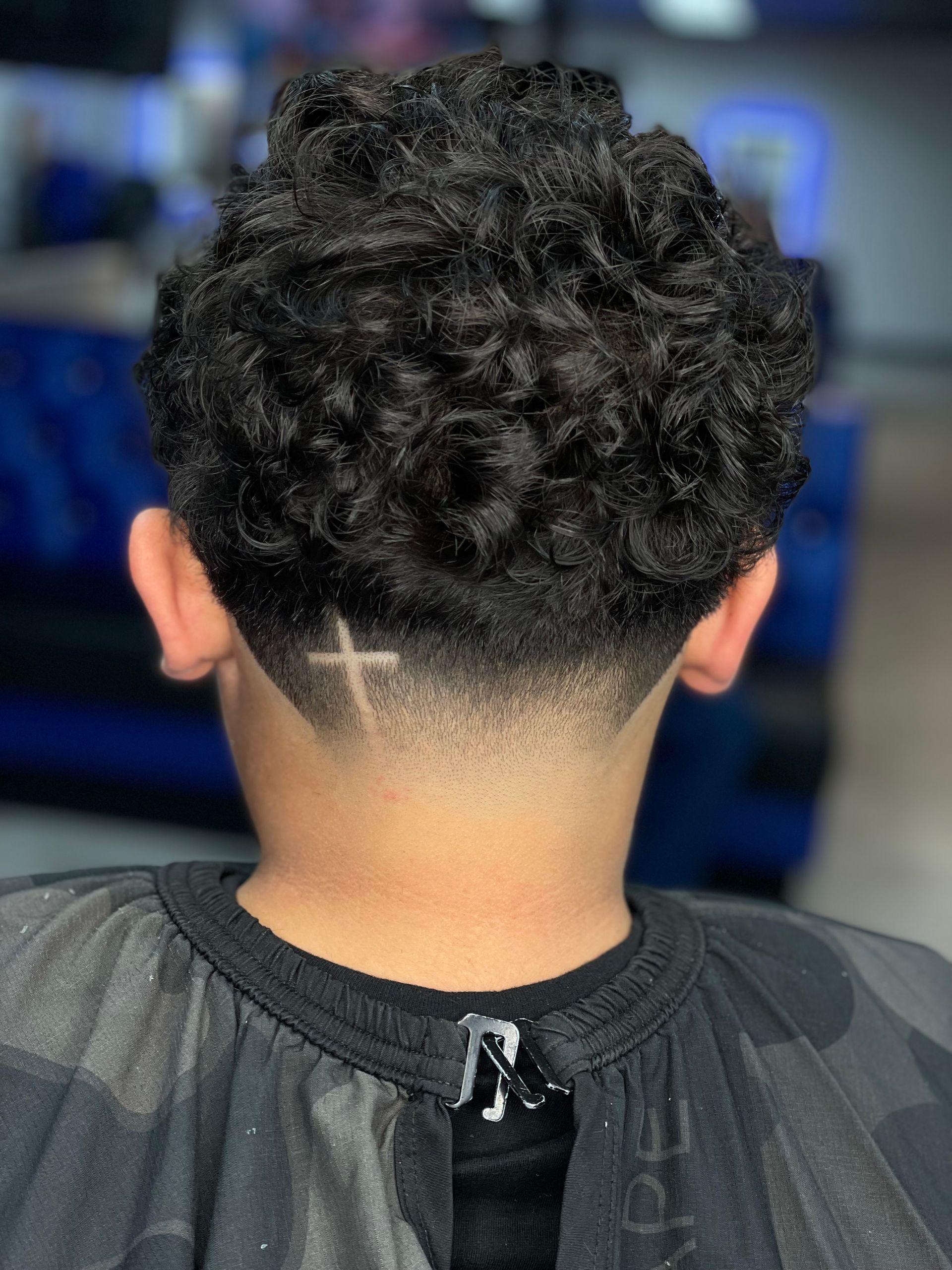 Boy with curly black hair, faded nape, and a cross design.