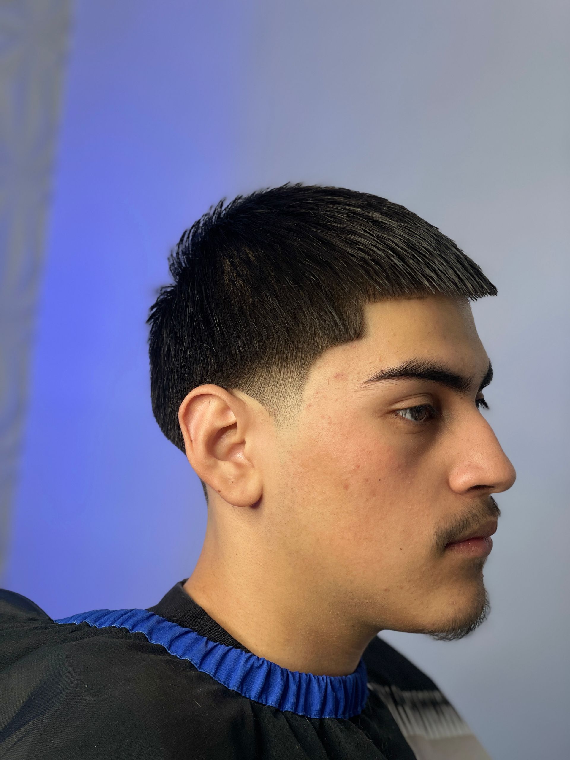 Man with a dark, short haircut, faded on the sides. Profile shot with blue background.