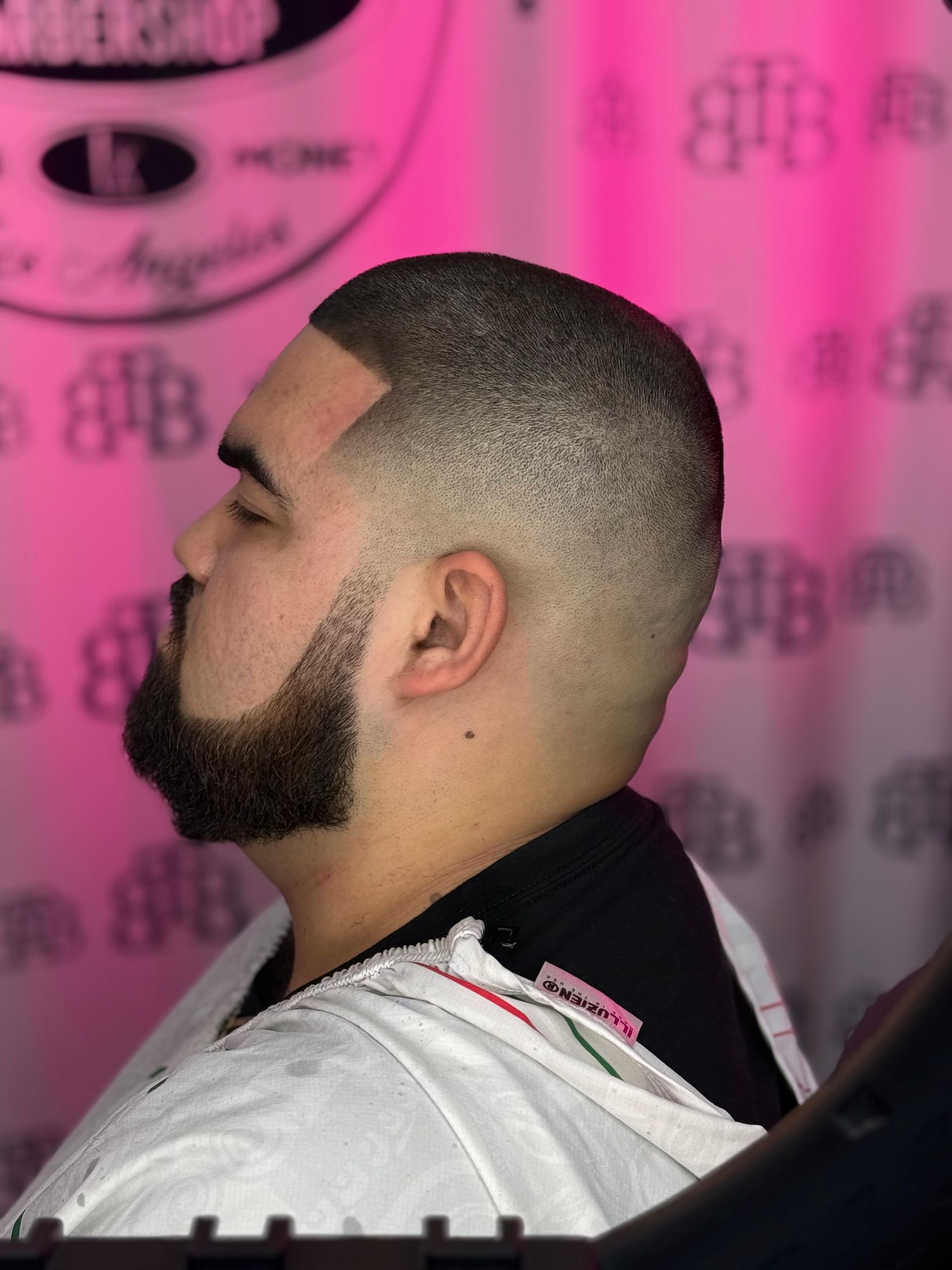 Man with faded haircut and beard; side profile in a pink setting.