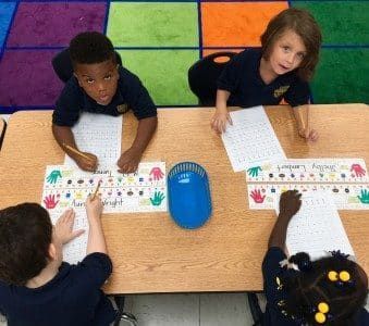 A group of children are sitting at a table writing on paper.