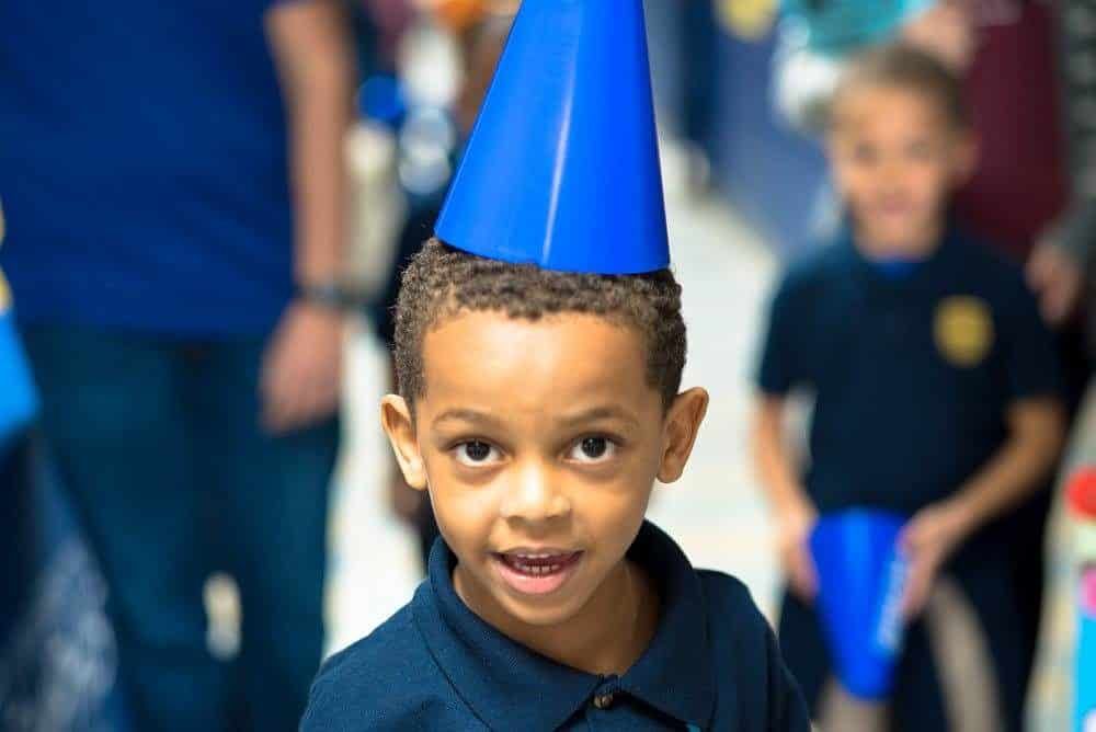 A young boy wearing a blue party hat is smiling for the camera.