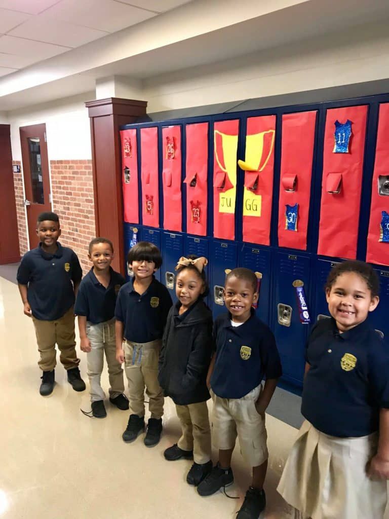 A group of children are standing in front of a row of lockers.
