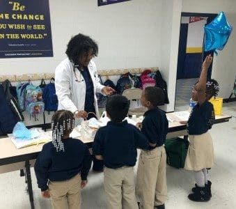 A group of children are standing around a table with a doctor holding a blue balloon.