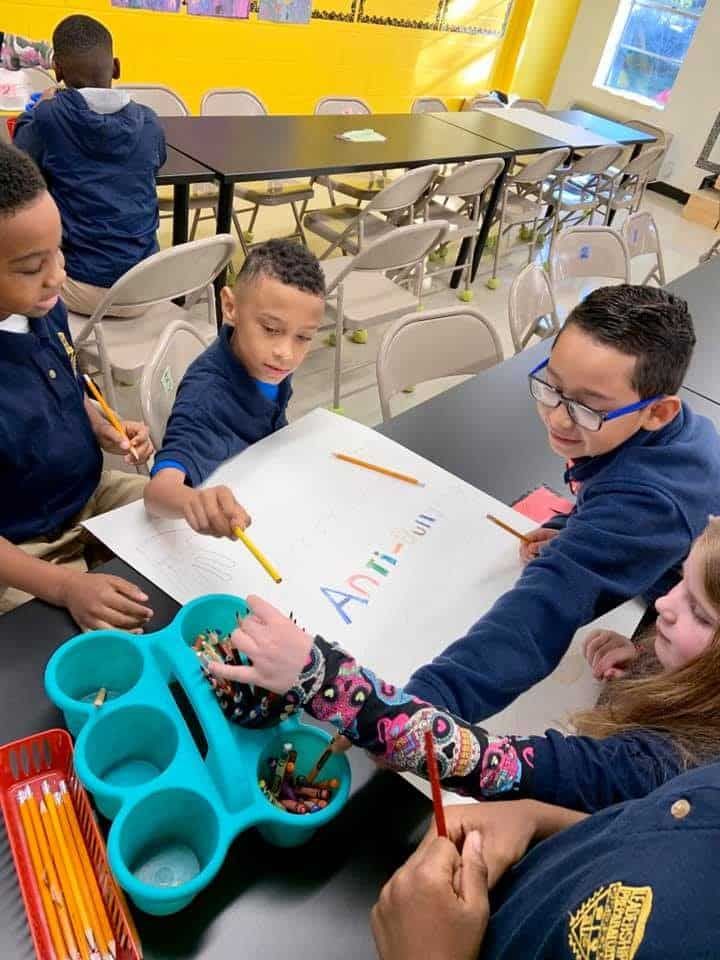 A group of children are sitting at a table writing on a piece of paper.