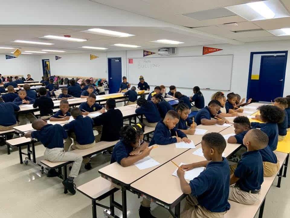 A group of children are sitting at tables in a classroom.