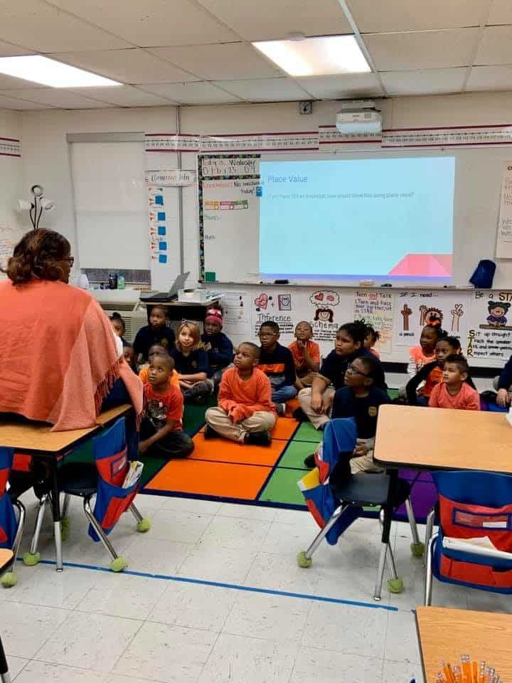 A woman is standing in front of a group of children in a classroom.