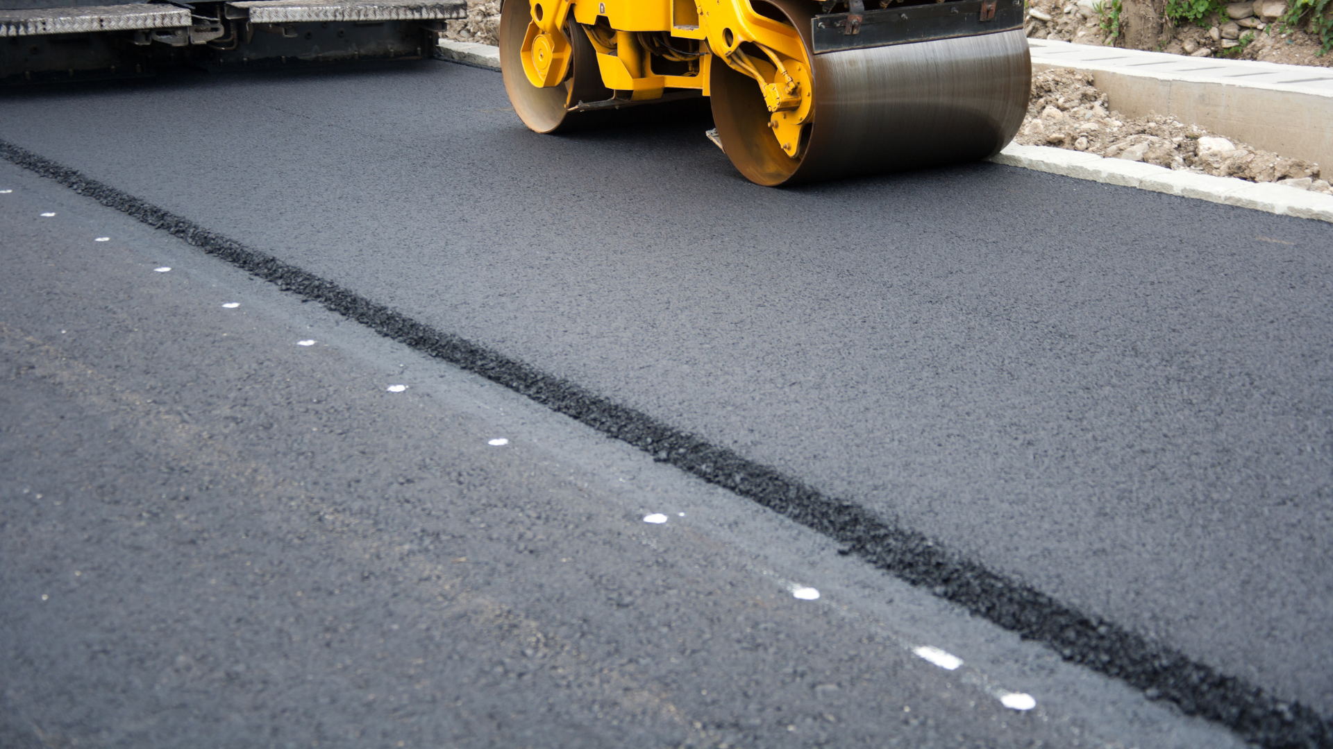 A yellow roller is rolling asphalt on a road.