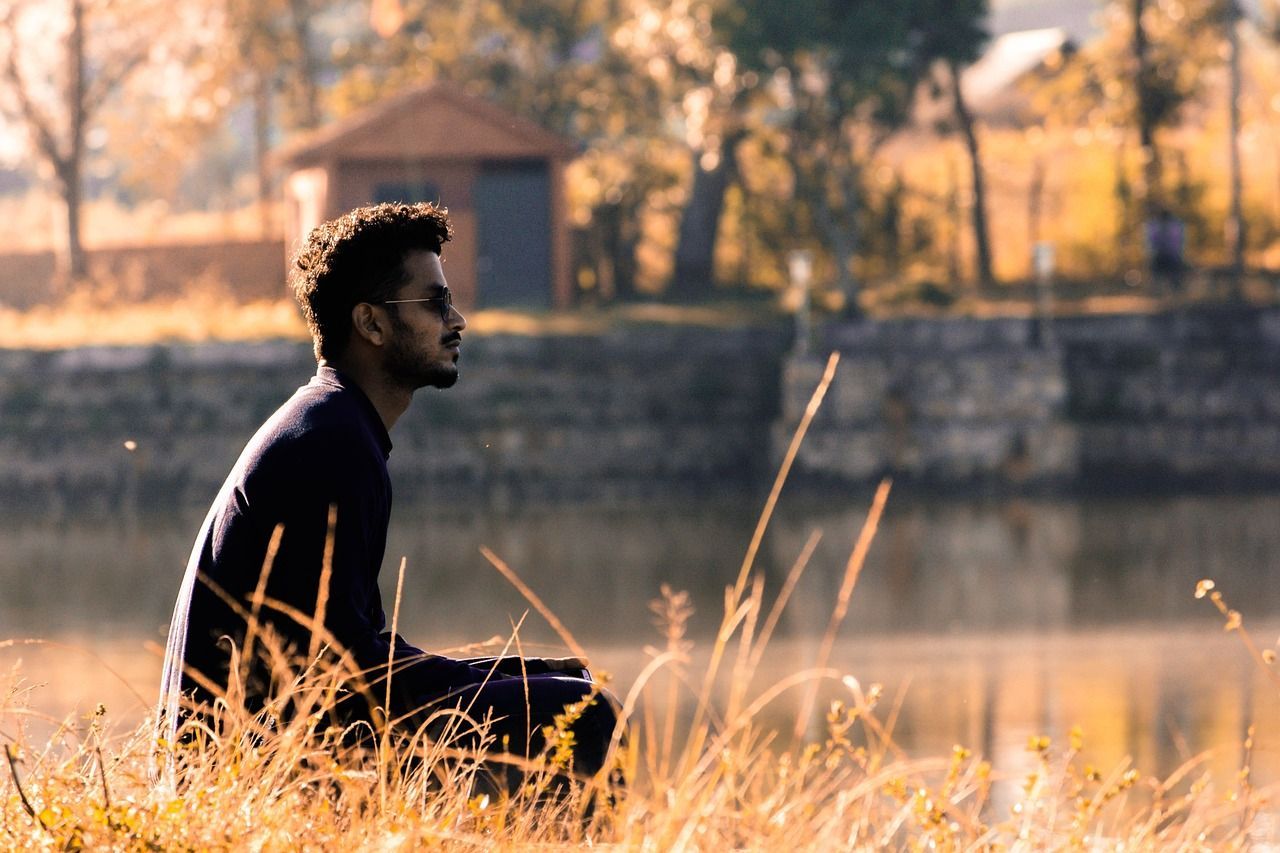 A man is sitting in the grass near a lake.