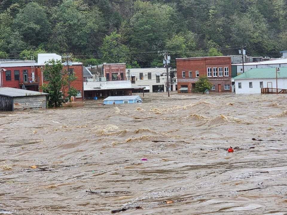 Floodwater engulfs buildings in a town, brown water, overcast sky.