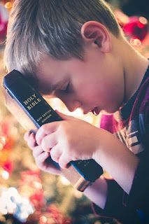 A young boy is holding a bible in front of a christmas tree.
