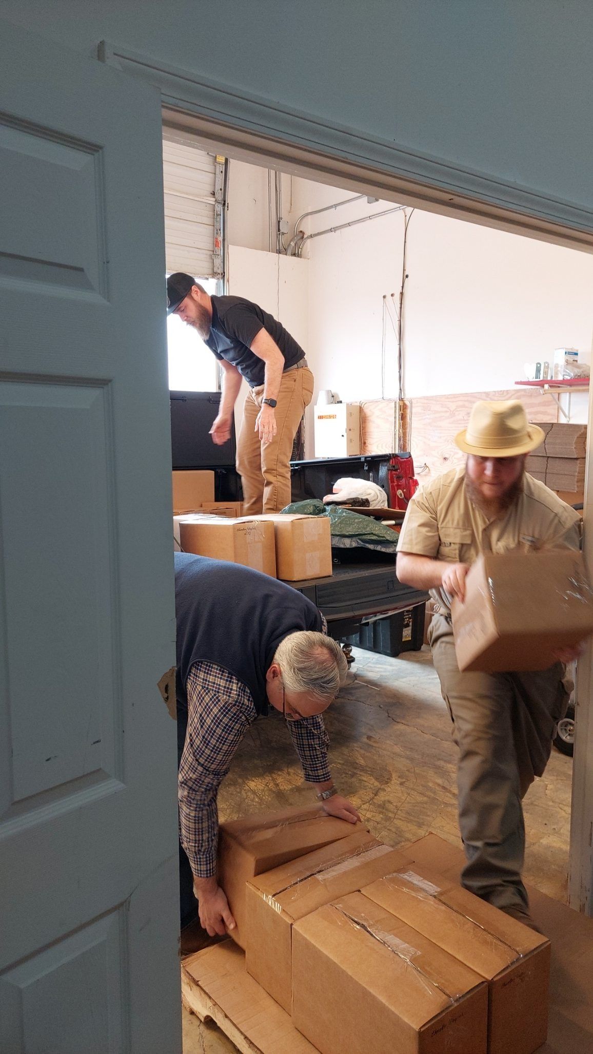 People loading boxes into a warehouse. Men and women working in a garage, moving cardboard boxes.