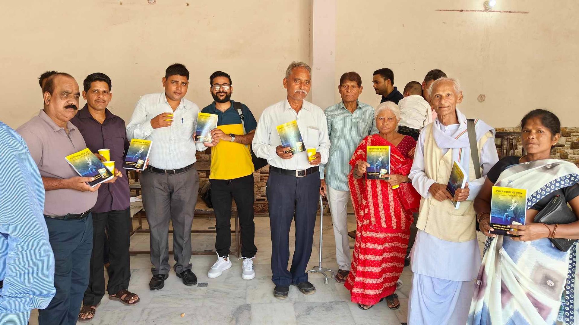 Group of people holding books, likely at a book distribution event, inside a room.