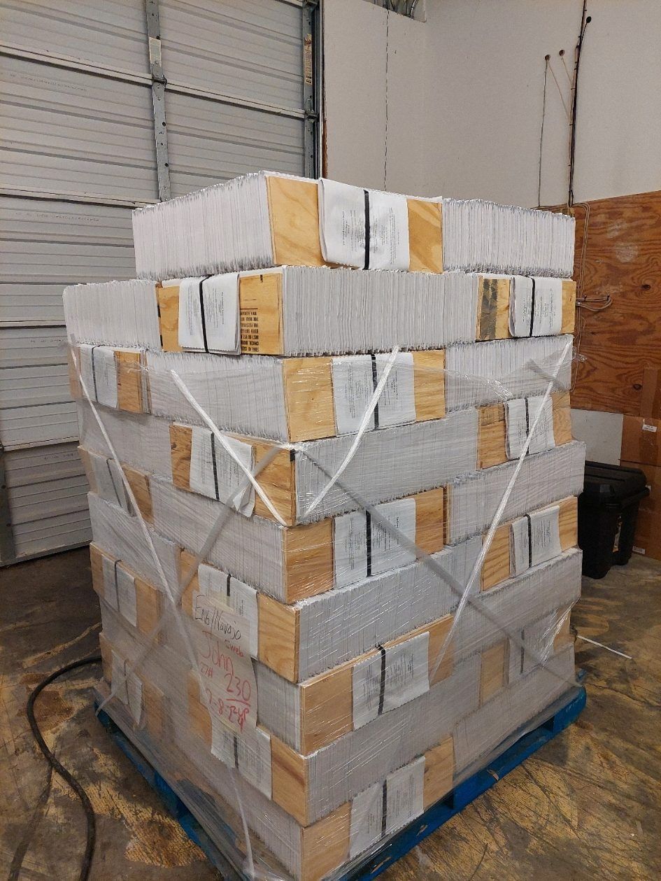 Pallet of stacked white tiles wrapped in clear plastic inside a warehouse.