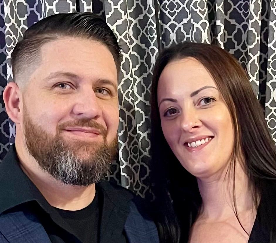 A man in a suit and a woman in a black dress are posing for a picture.