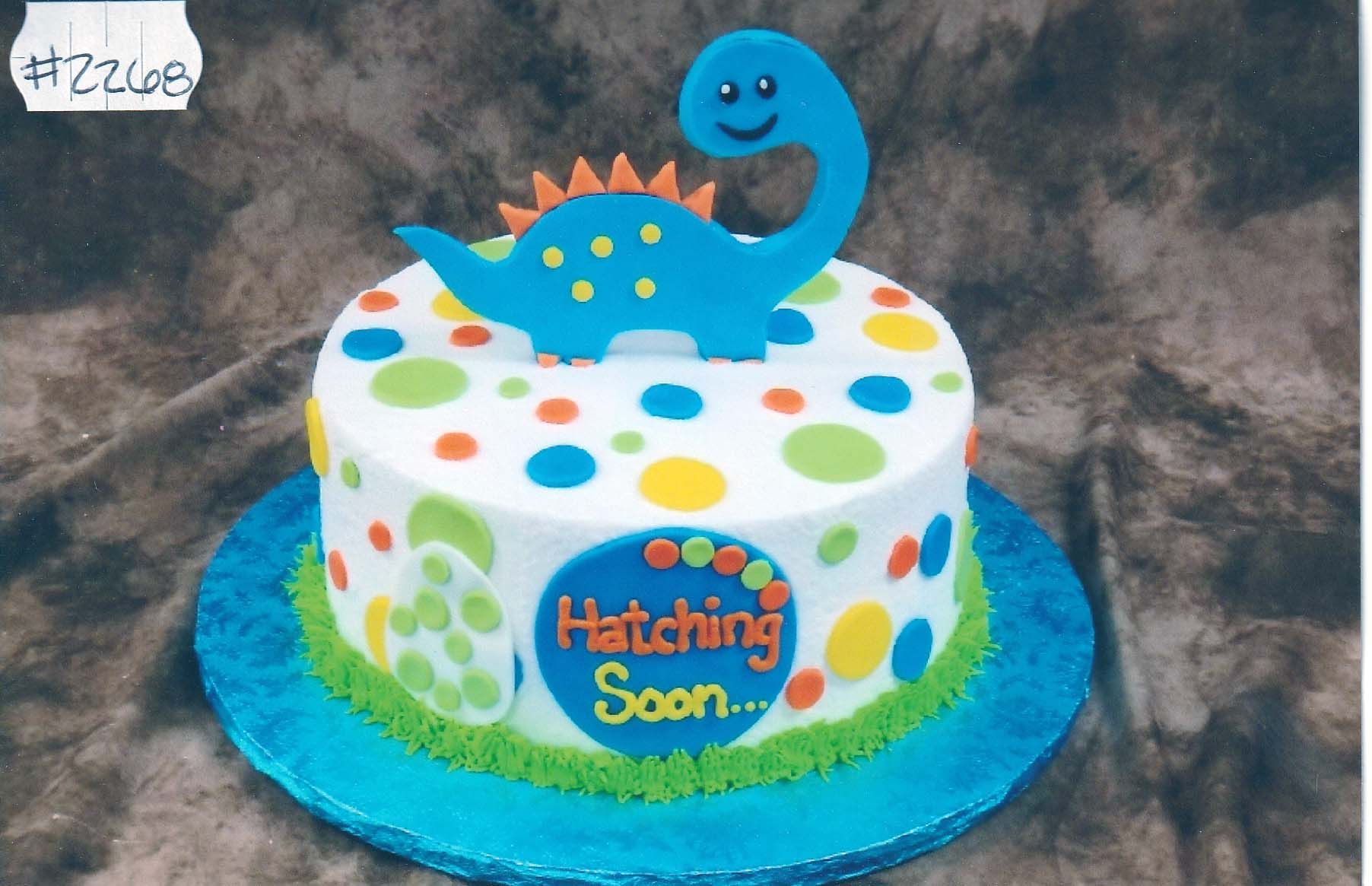 A cake with a dinosaur on top that says hatching soon