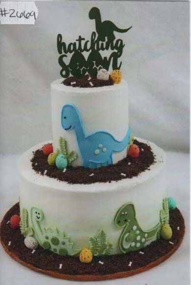 A cake with a dinosaur on top that says ' hatchling ' on it