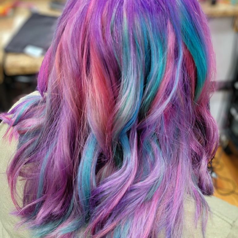 A woman with purple and blue hair is sitting in a chair.