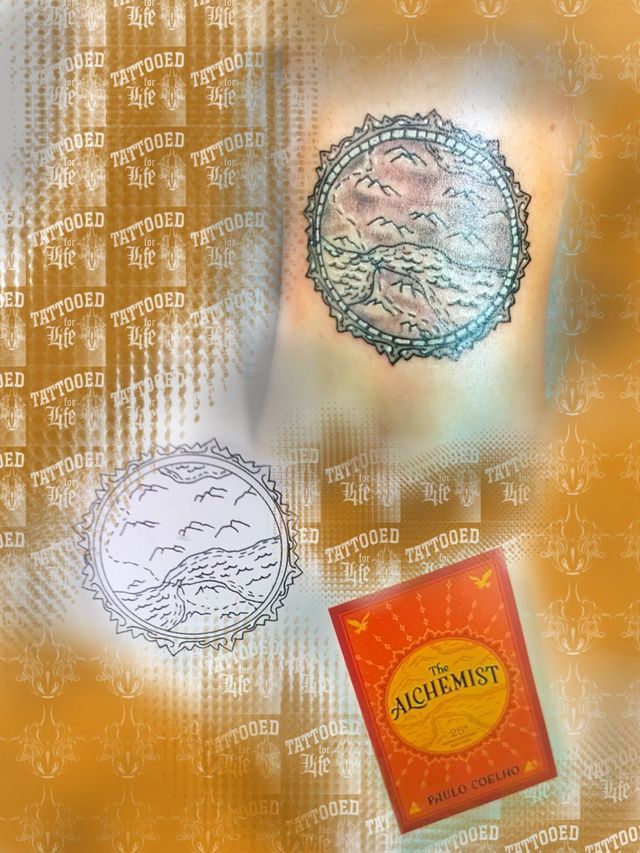 A book called the alchemist is on a table next to a tattoo.