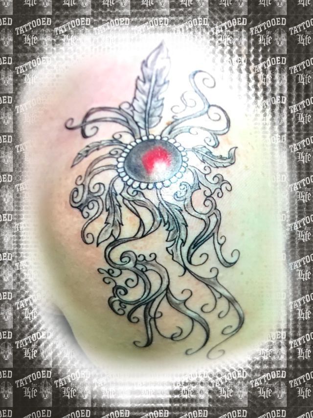 A tattoo of a feather with a red stone in the middle