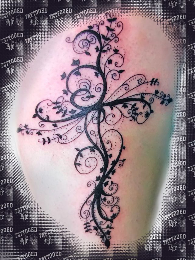 A tattoo of a cross with swirls and leaves