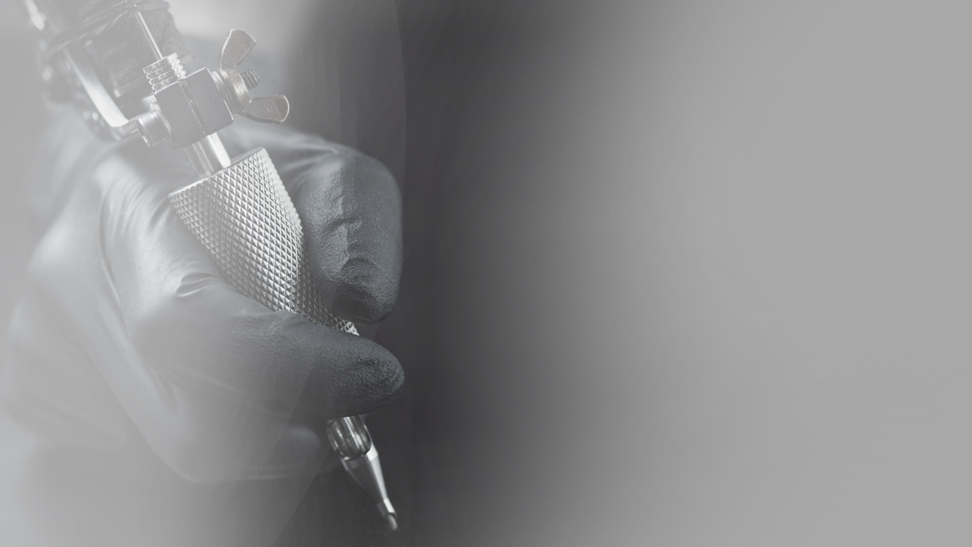 A person is holding a tattoo machine in their hand in a black and white photo.