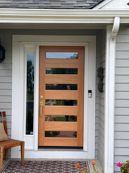Wooden front door with horizontal glass panels and sidelight, gray siding.