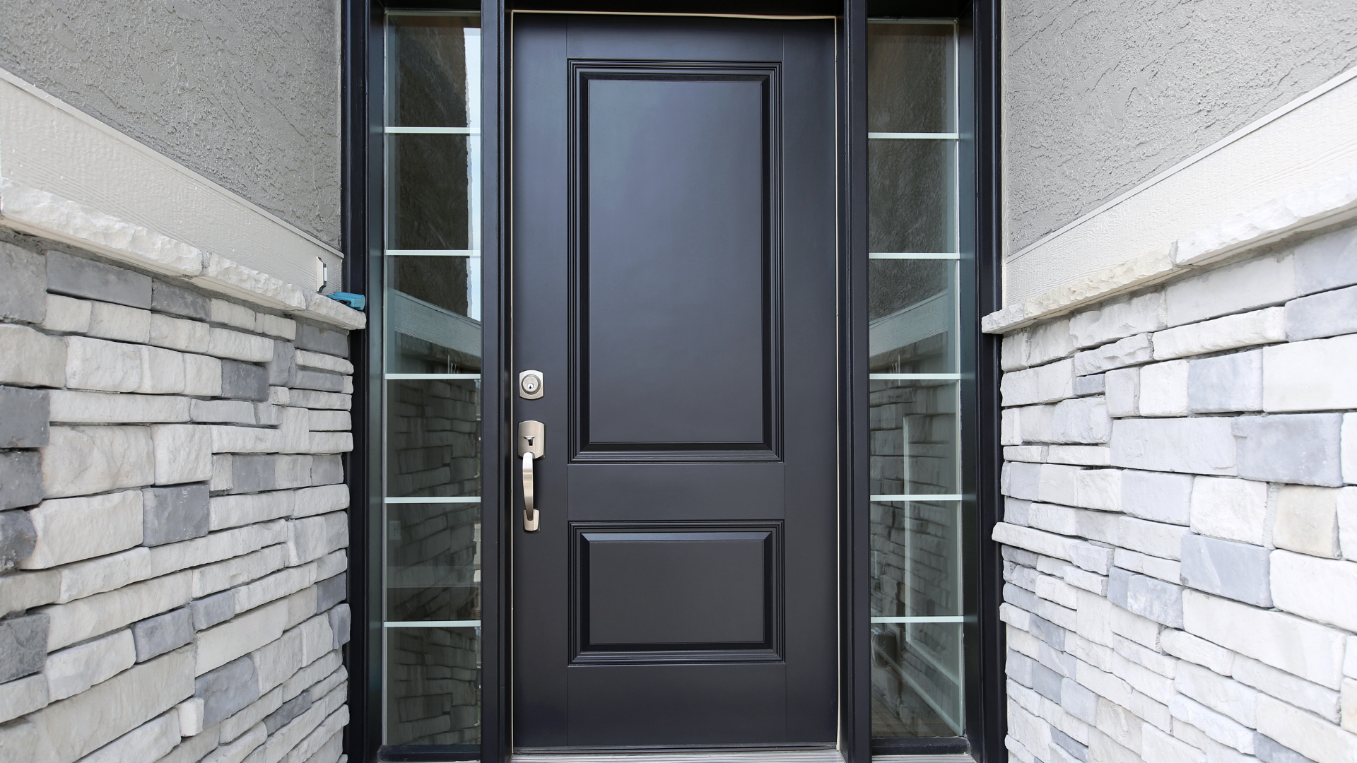 Black front door with sidelights, surrounded by stone and stucco, gold door handle.