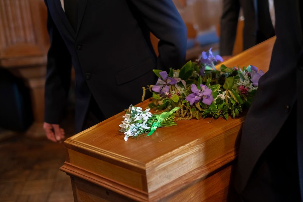 A man in a suit is sitting at a coffin at a funeral.