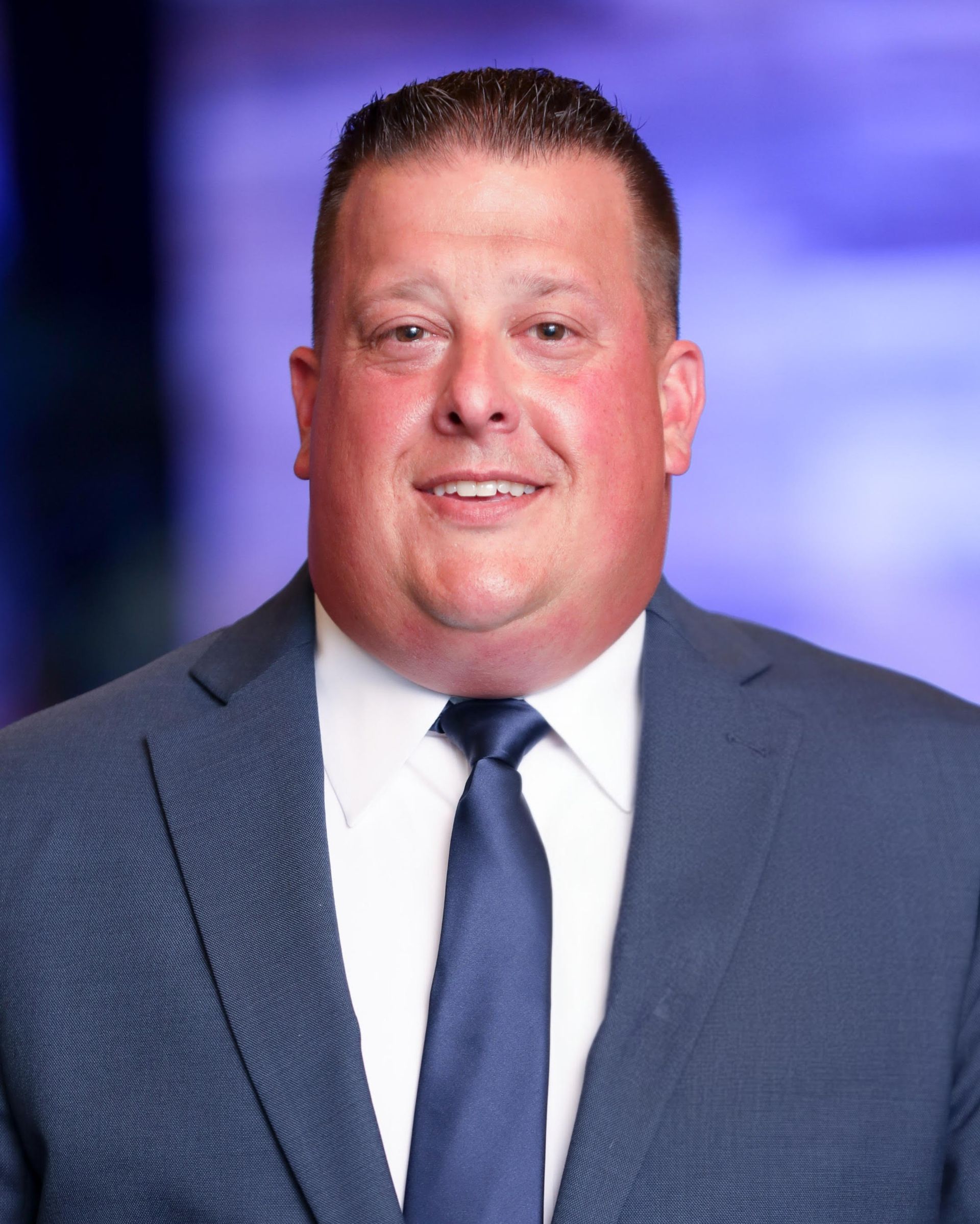 Two men in suits smiling, one with a yellow tie, the other with a striped tie.