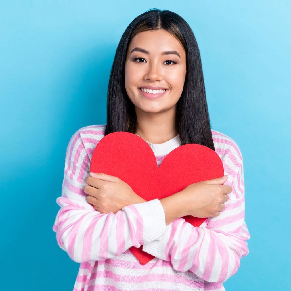 A woman in a pink and white striped sweater is holding a red heart.