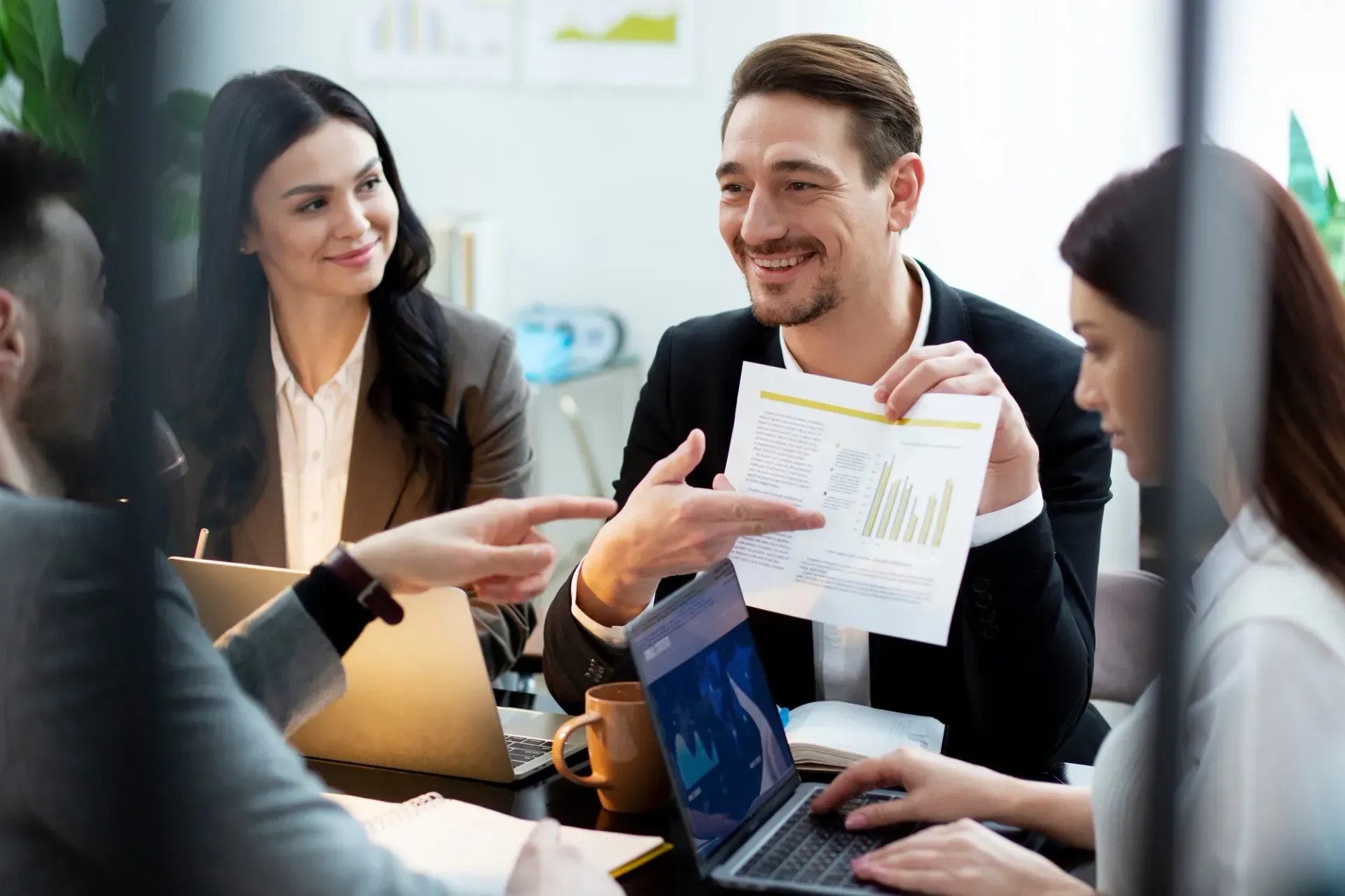 Business team in a meeting, reviewing documents and a laptop, smiling.