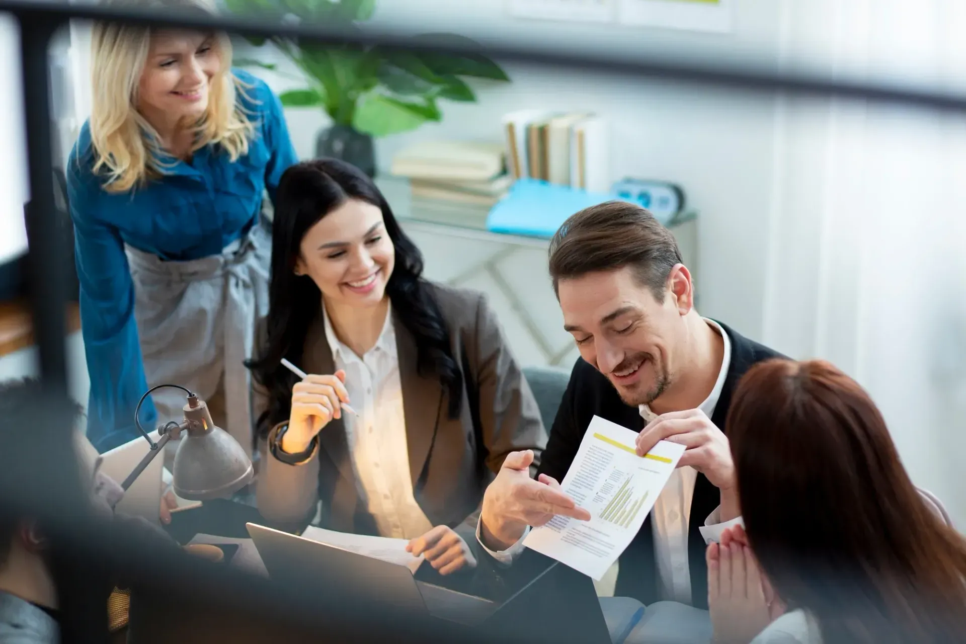 Four people in an office looking at documents and smiling. One person points at a paper.
