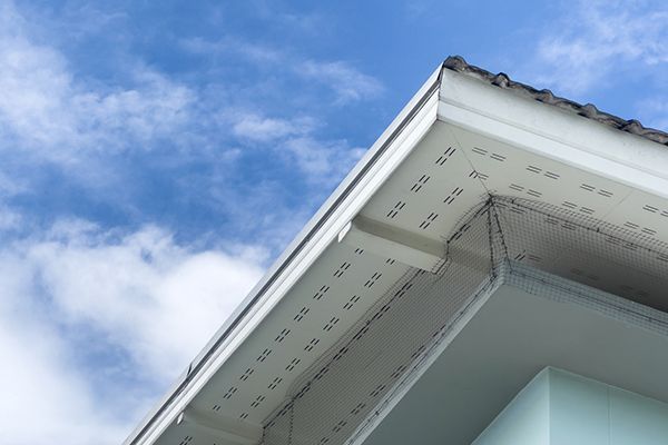 White house corner with gutters against a blue sky with clouds. White house corner with gutters against a blue sky with clouds.