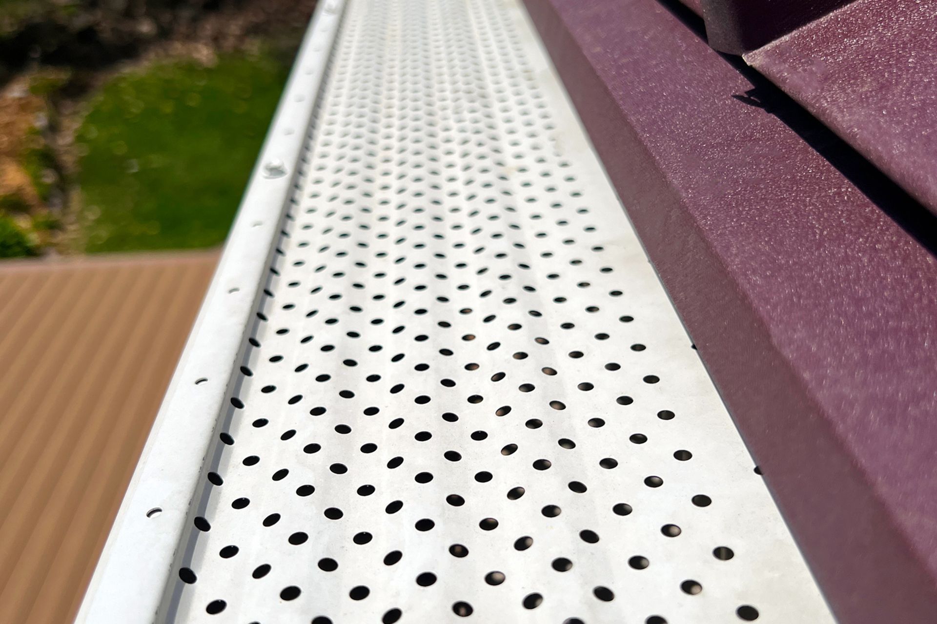 White gutter guard with small holes, alongside a purple roof edge. White gutter guard with small holes, alongside a purple roof edge.