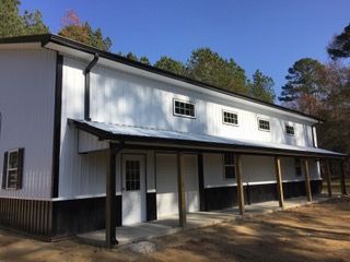 Two-story white and black barn-style building with a porch, windows, and black roof.