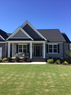 House exterior with gray siding, black shutters, and a well-manicured lawn under a clear blue sky.