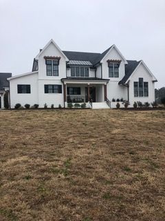 White two-story house with black trim, a covered porch, and brown grass.