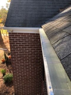 Gutter with a leaf guard on a brick wall beneath a dark gray shingled roof.