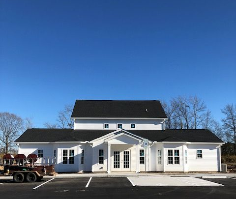 White gutter system with a downspout on a roof. White building with black roof, double doors, and parking lot on a sunny day.