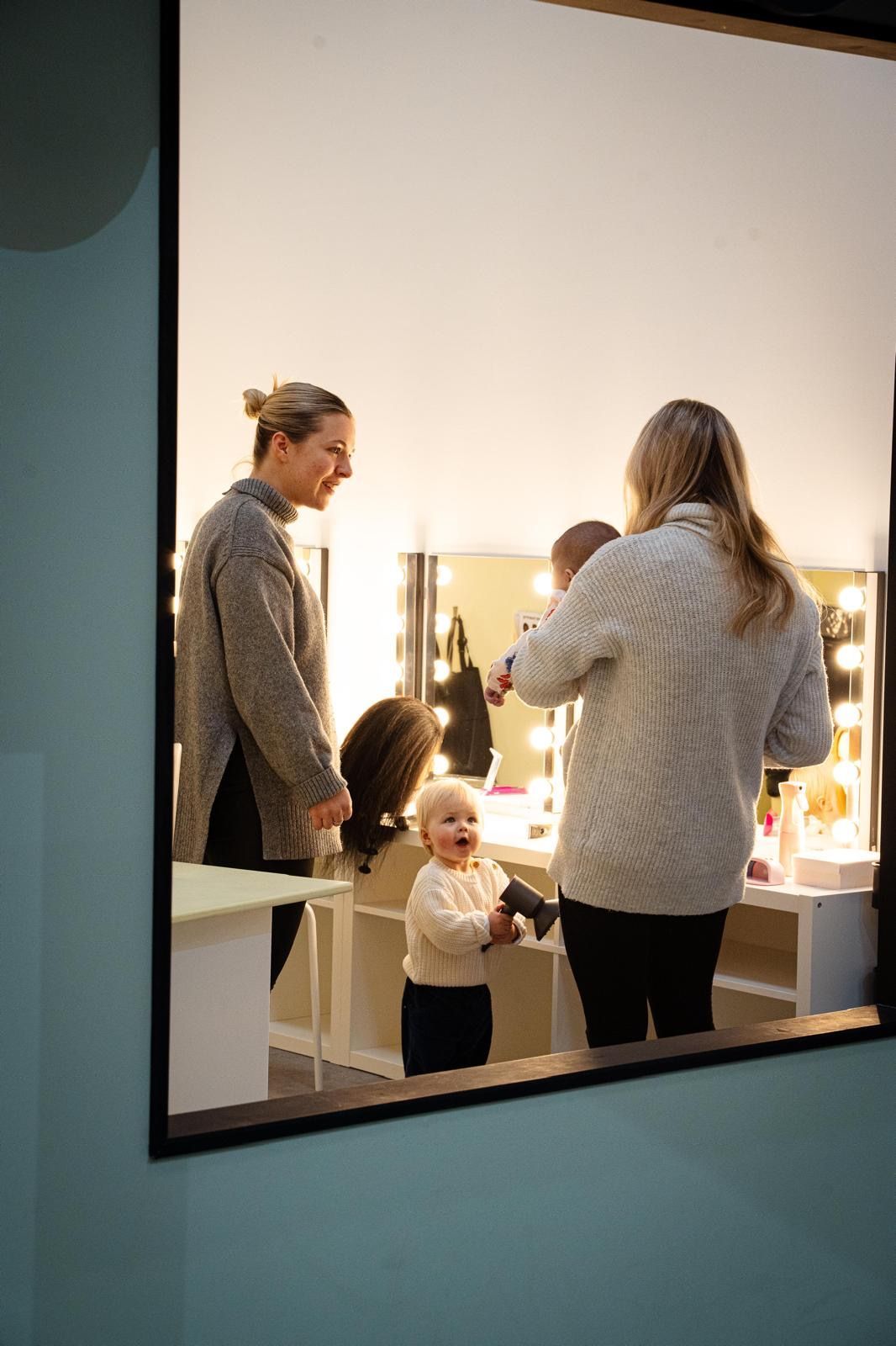 A woman is blow drying a child 's hair in front of a mirror.
