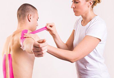 Uma mulher está colocando fita kinesio rosa no ombro de um homem.