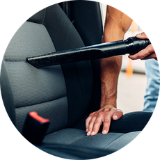 A man is cleaning the seats of a car with a vacuum cleaner.